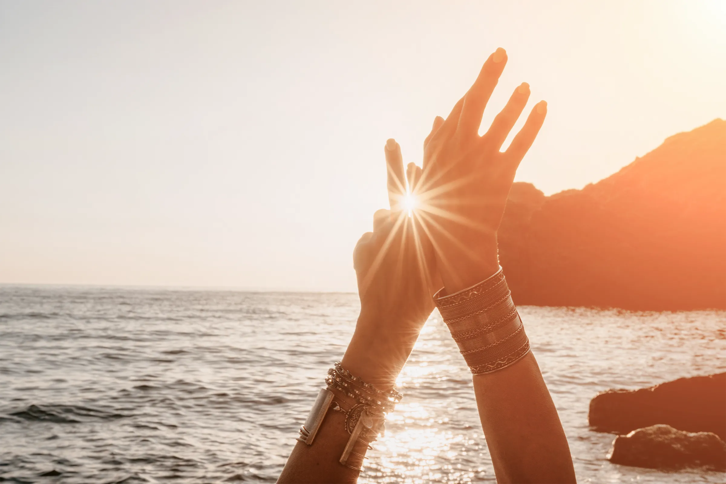 Erhobene Hände im Sonnenlicht am Meer.